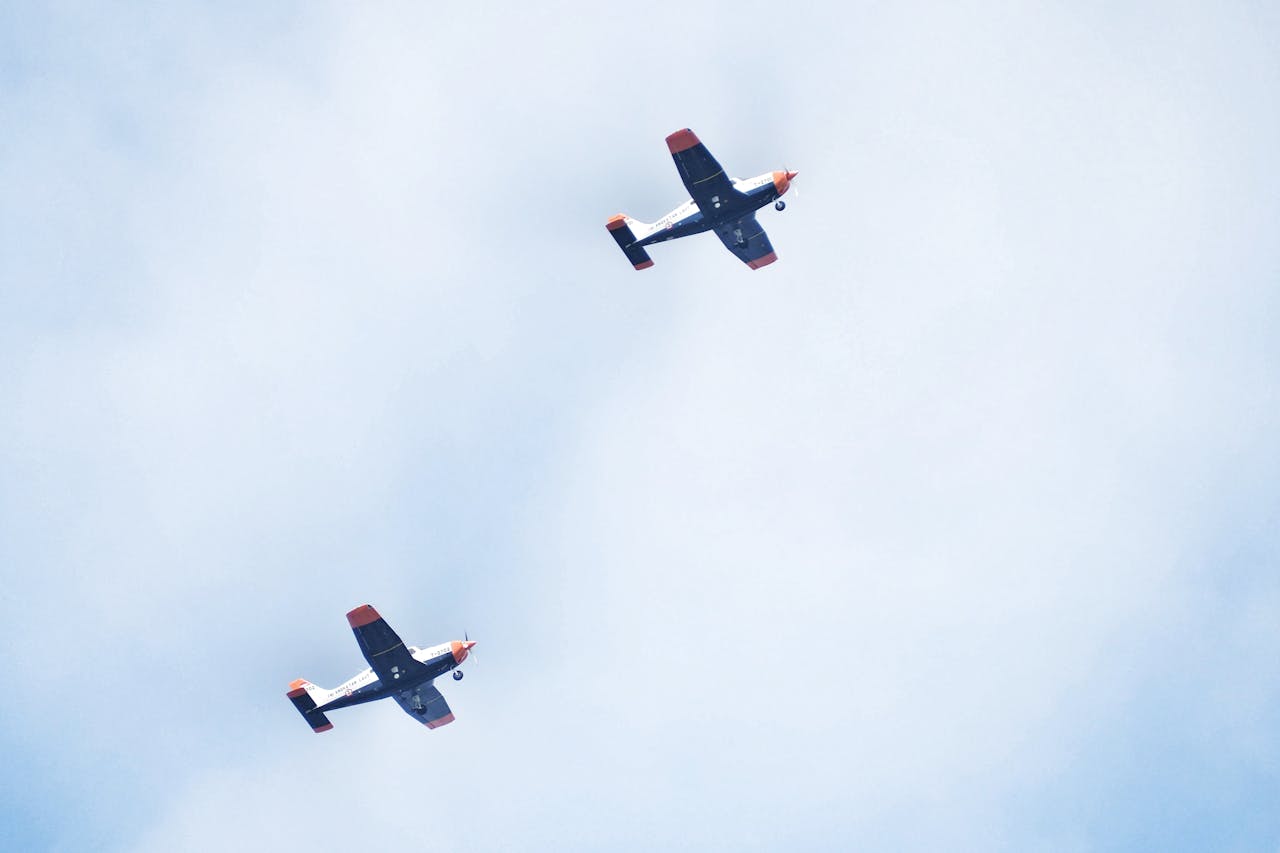gallery-3 Two small aircraft flying in formation against a cloudy sky, showcasing aerial coordination.