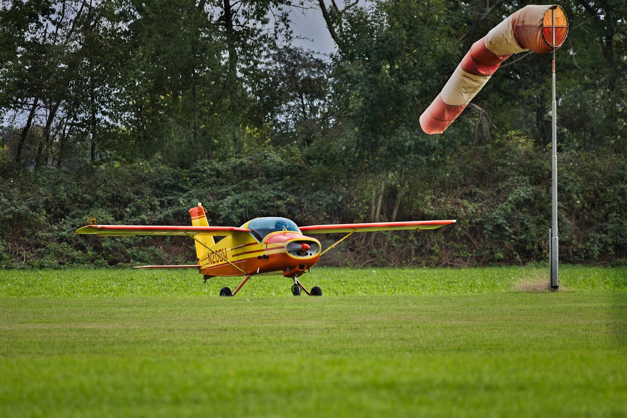our-services-1 A small yellow airplane on a grassy field with a windsock swaying in the breeze.